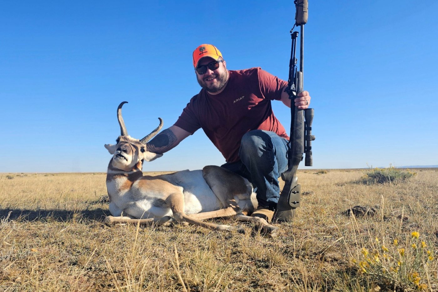 Brian Dimoff kneeling with his rifle beside a harvested pronghorn on the prairie