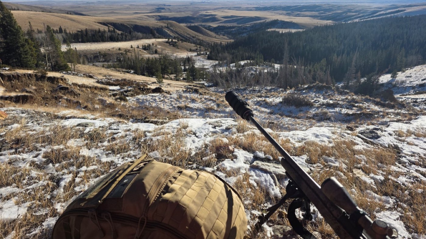 A scoped rifle on a bipod overlooking a snowy valley